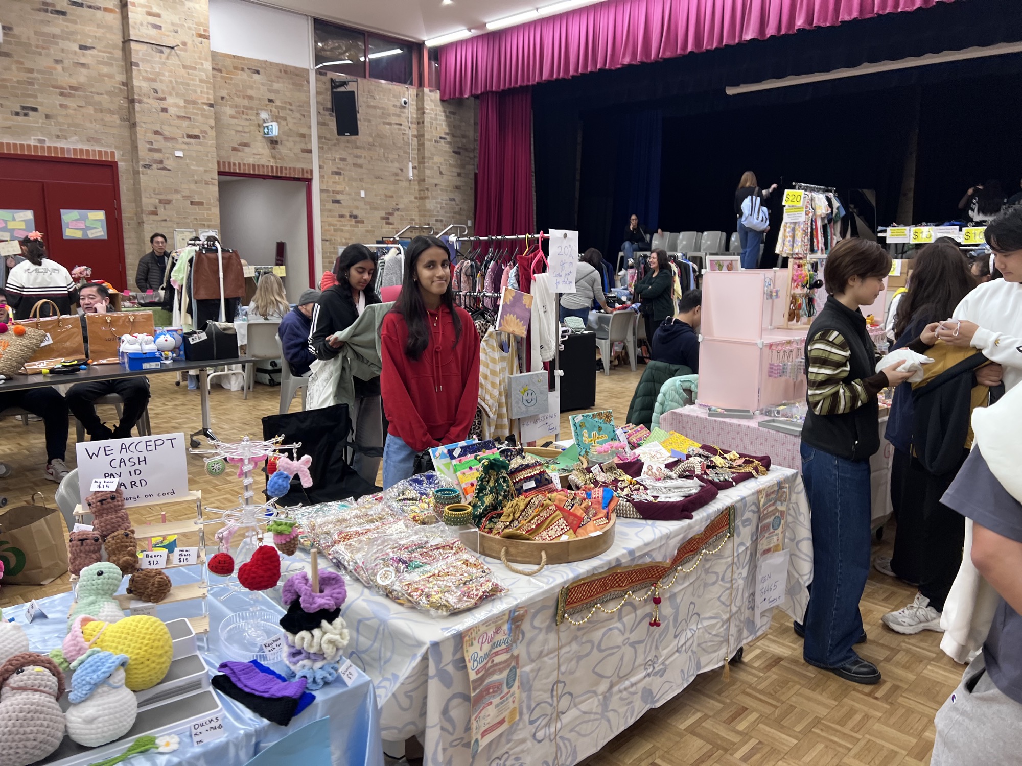 A stallholder in a red hoodie behind a table of handmade jewellery, pouches and crochet pieces