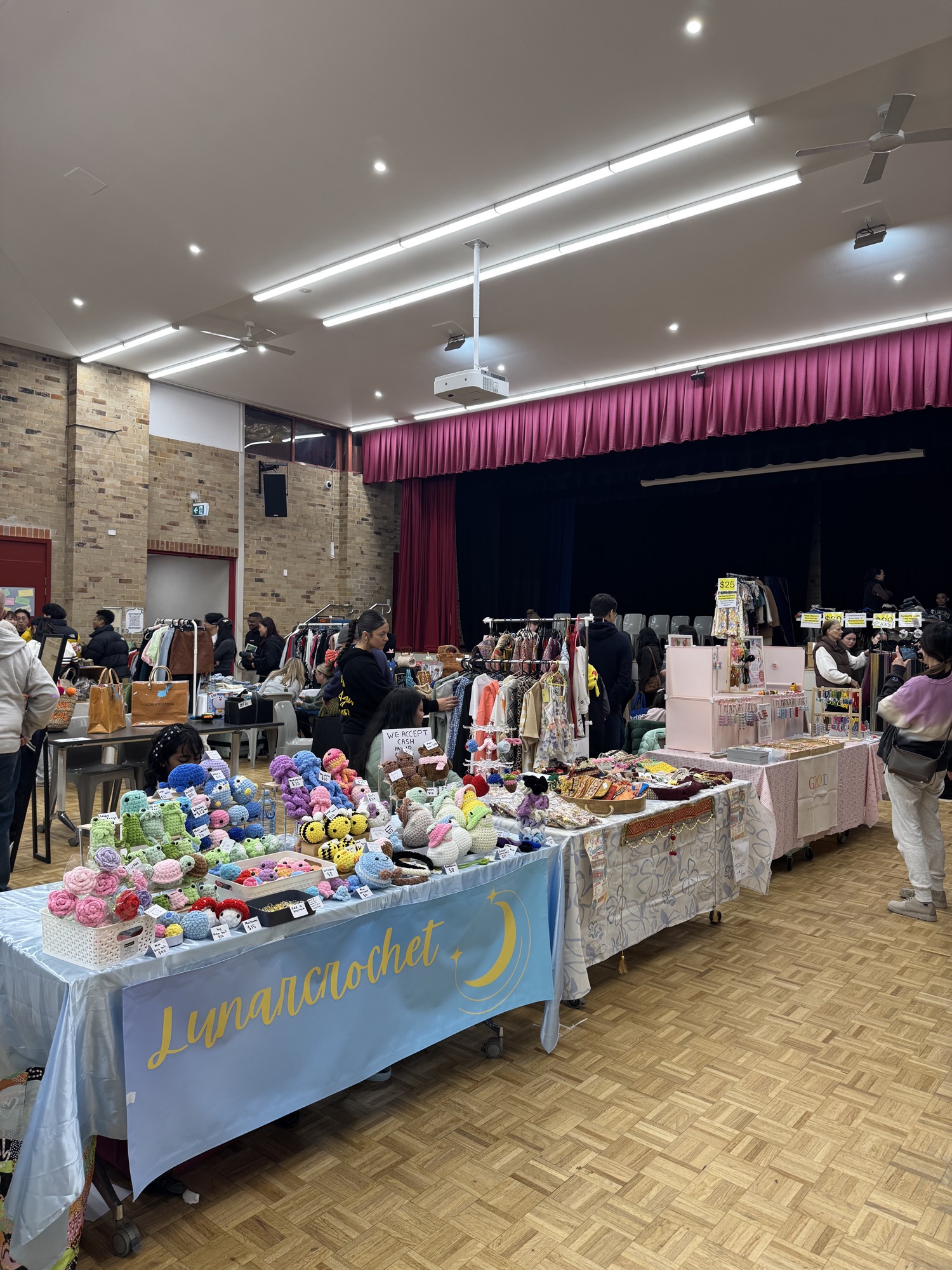 Wide view of the market floor with stallholders and shoppers beneath the stage