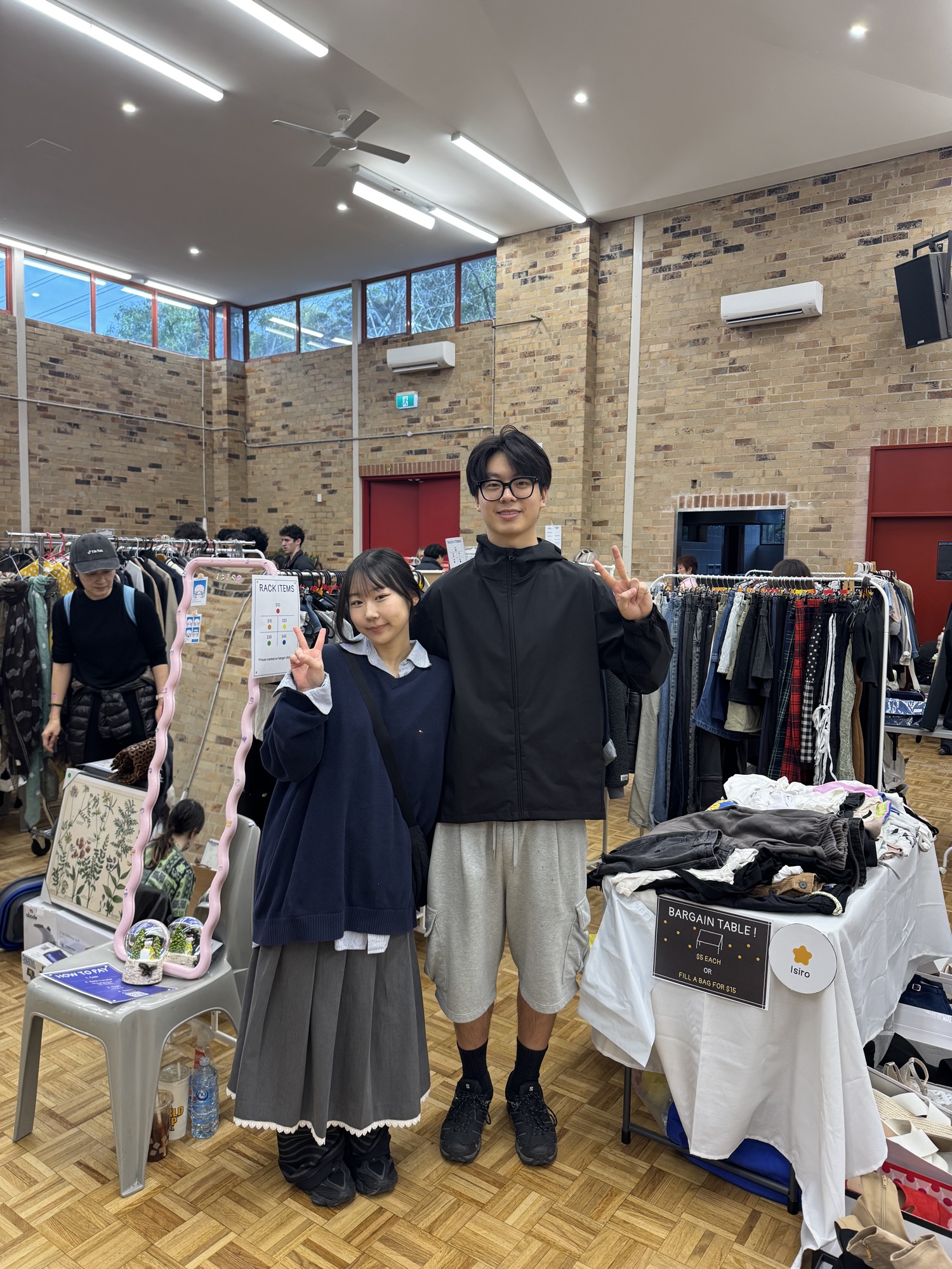 Two visitors posing beside a pre-loved clothing rack and bargain table