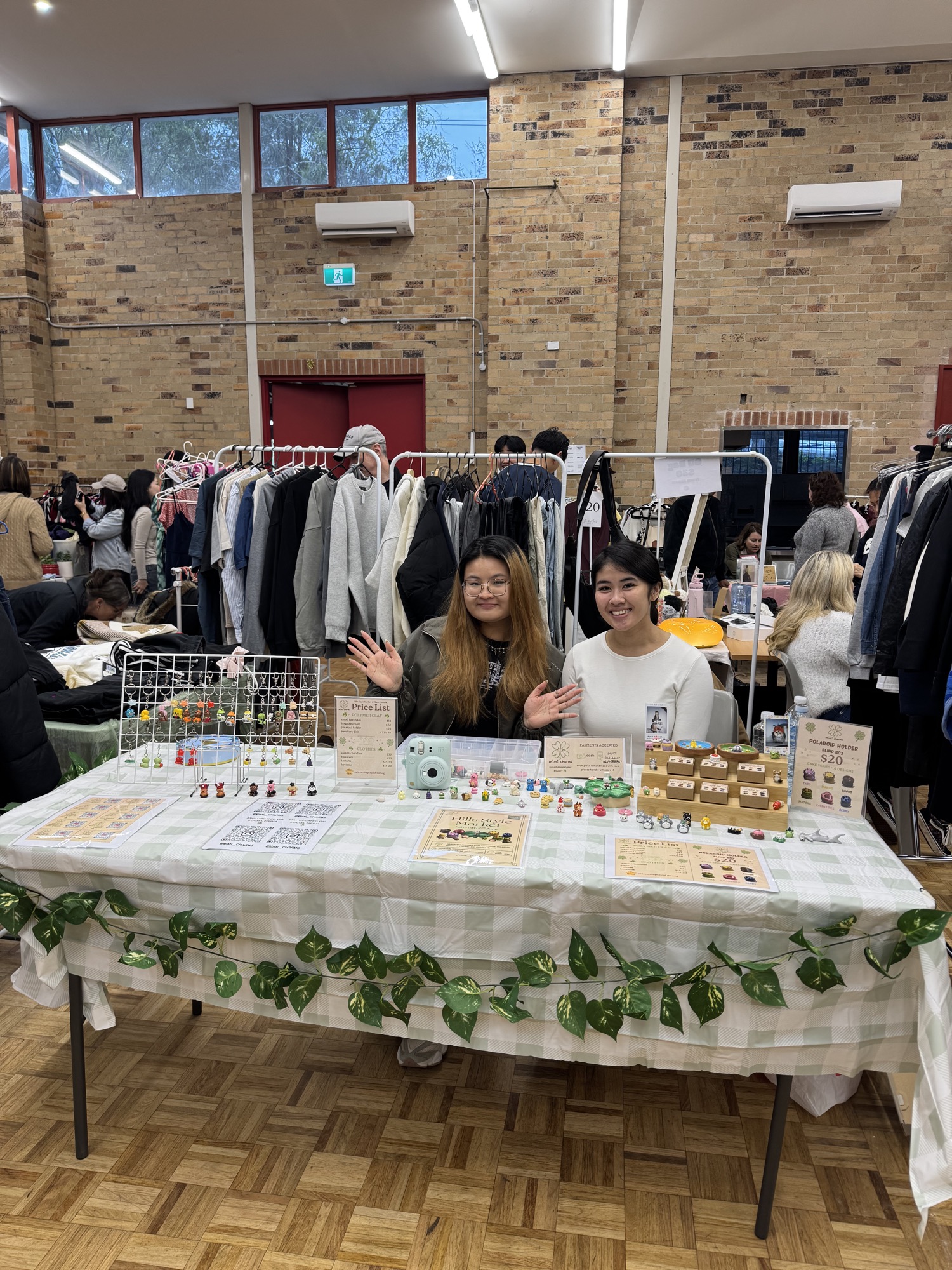 Two smiling stallholders behind a table of handmade polymer clay keychains and charms