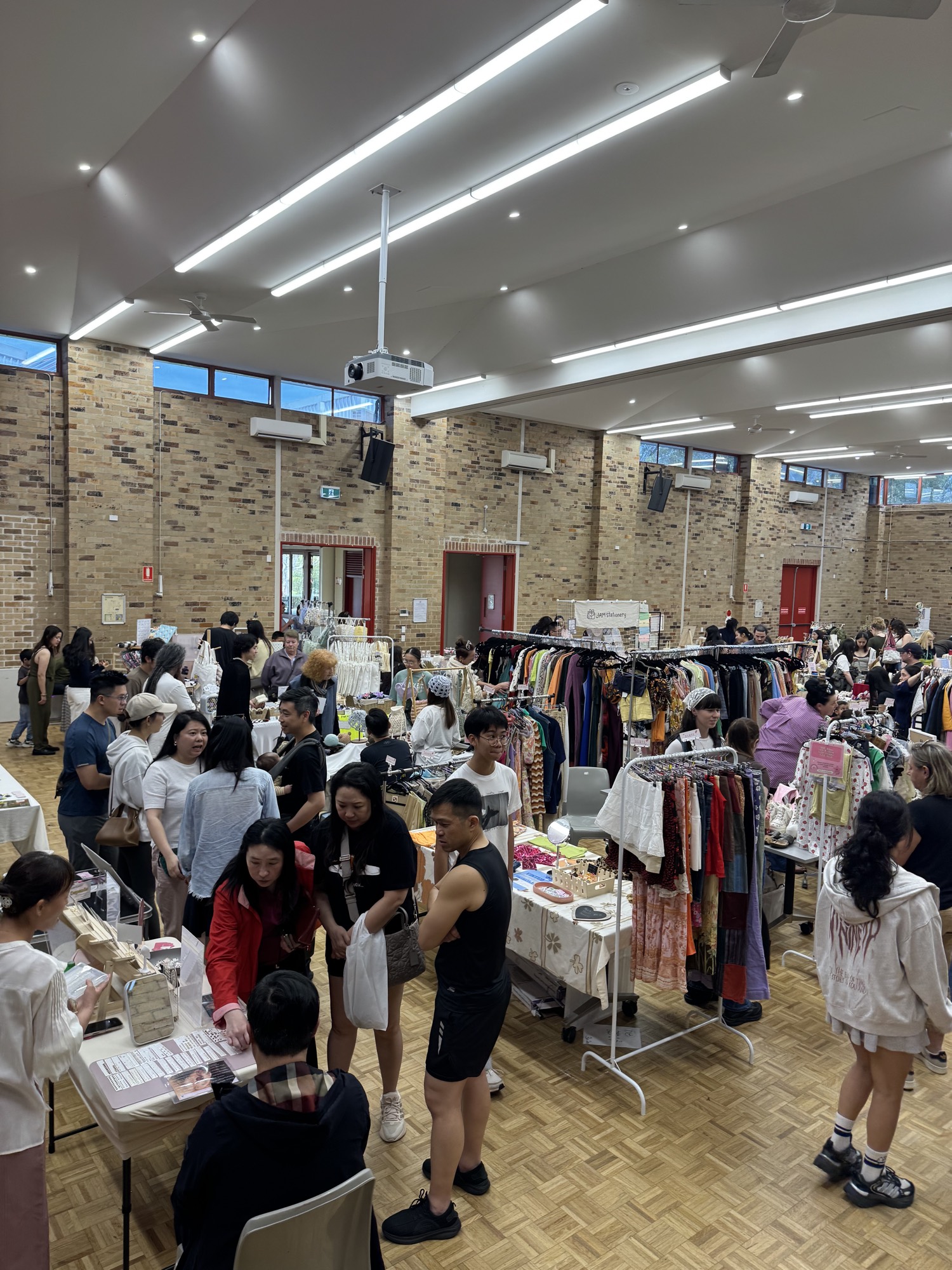 A busy aisle of the market, with visitors gathered around clothing racks and handmade stalls