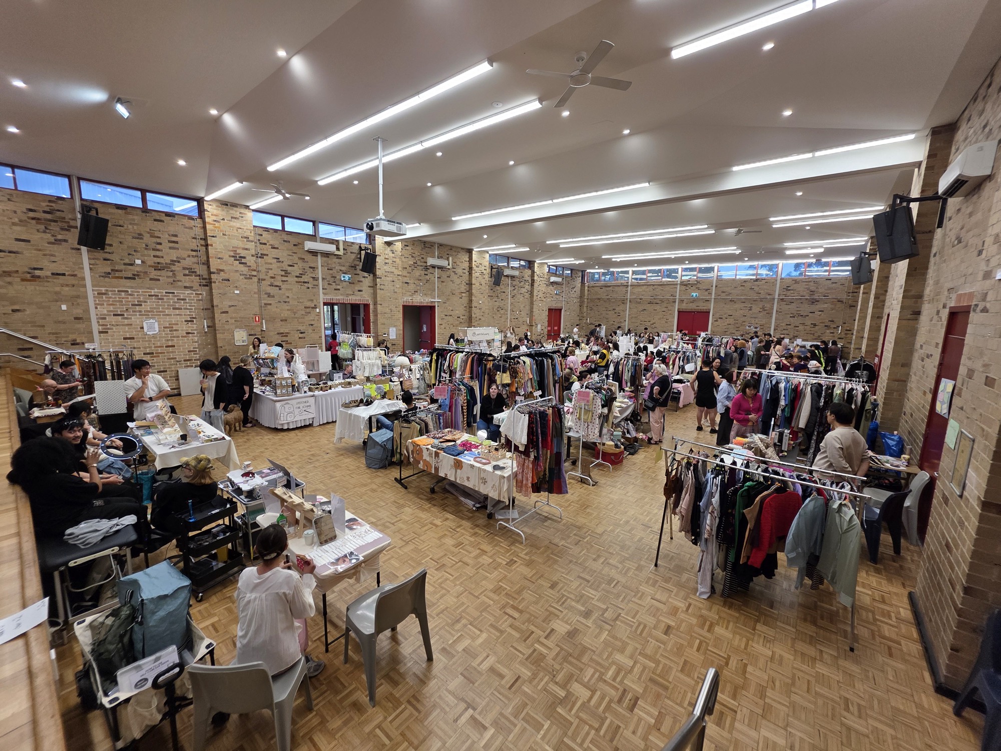 A wide view from the mezzanine over clothing racks, stall tables and visitors on the market floor